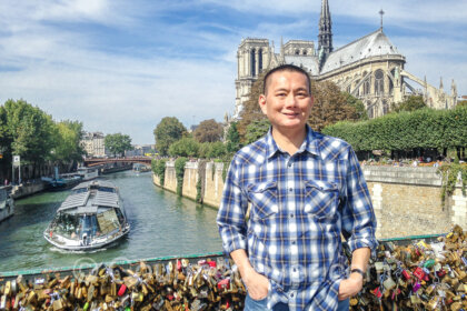 The Gourmet Flyer posing with a river cruise boat and Notre Dame Cathedral in the background.