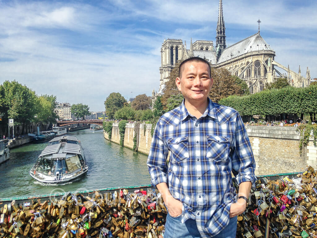 The Gourmet Flyer posing with a river cruise boat and Notre Dame Cathedral in the background.