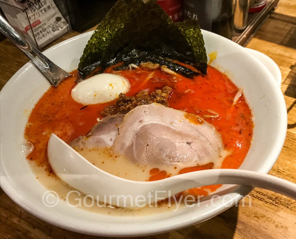 A bowl of ramen with milky pork broth topped with a layer of red chili oil.