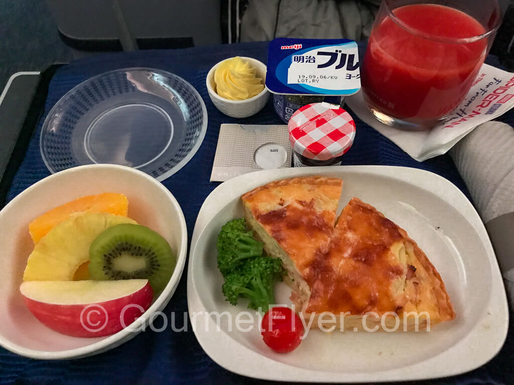A breakfast tray with a quiche, fruits, and togurt.