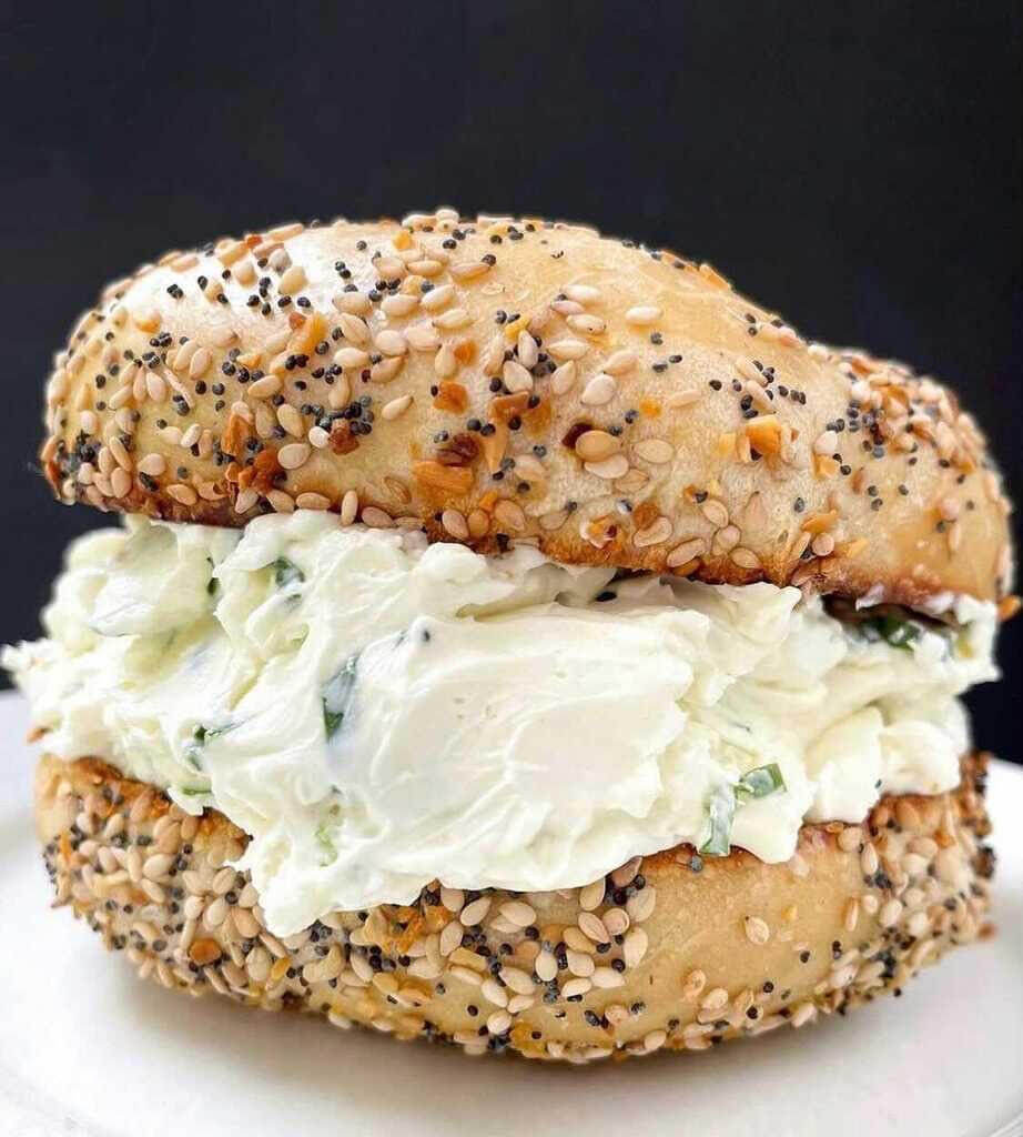 A sesame seed bagel is loaded with a thick slab of cream cheese.