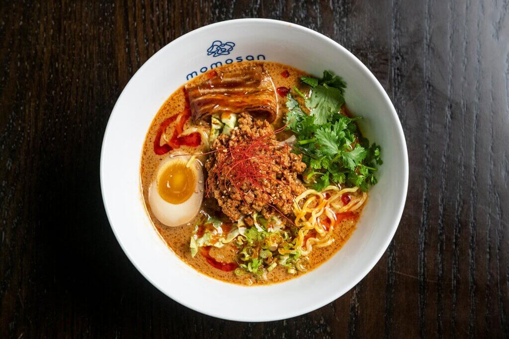 A bowl of spicy tan tan noodles with ground pork and half a boiled egg.