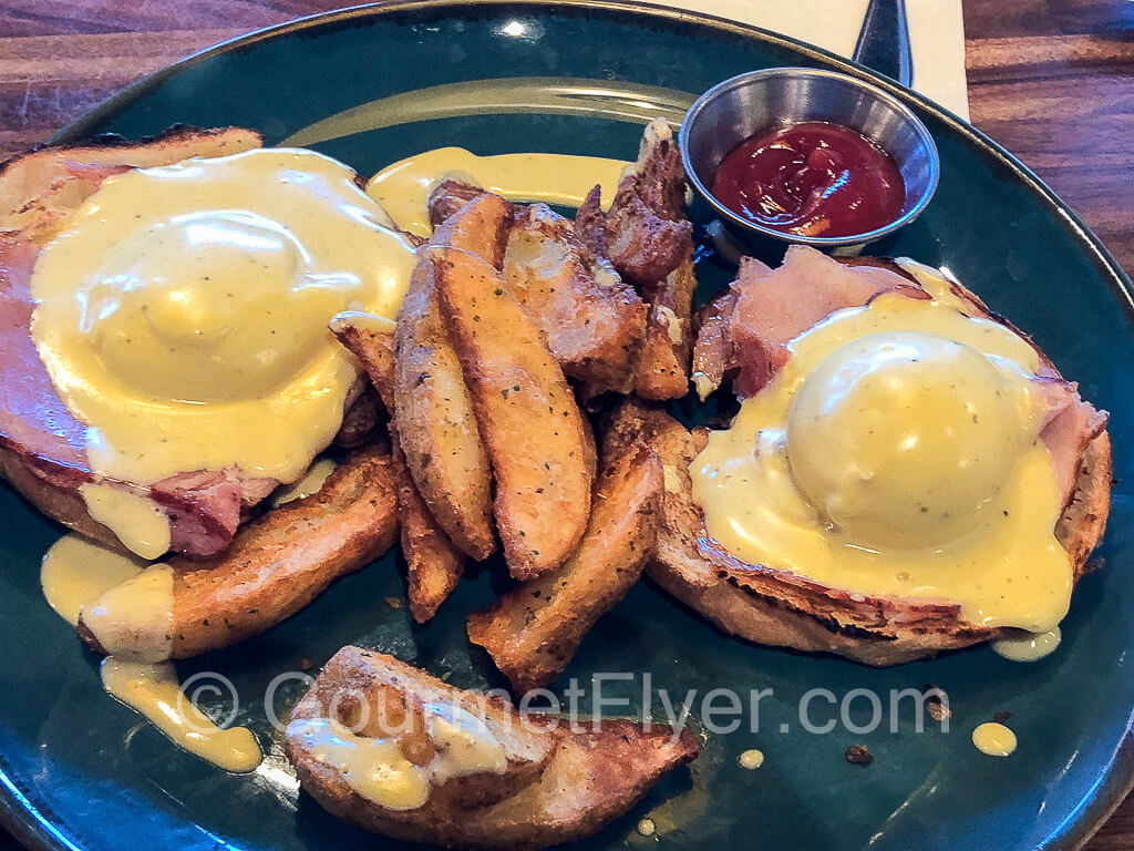 A pair of egg benedicts are served with duck fat fries between them.
