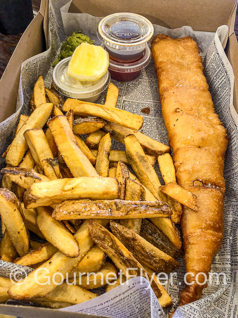 Fish and chips served in a to-go box with condiments.