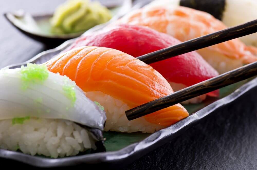 A platter of sushi combo with a pair of chopsticks picking up a salmon sushi.