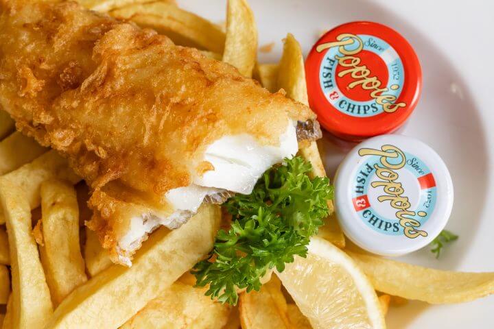 A plate of fish and chips with dipping sauces and a lemon wedge.