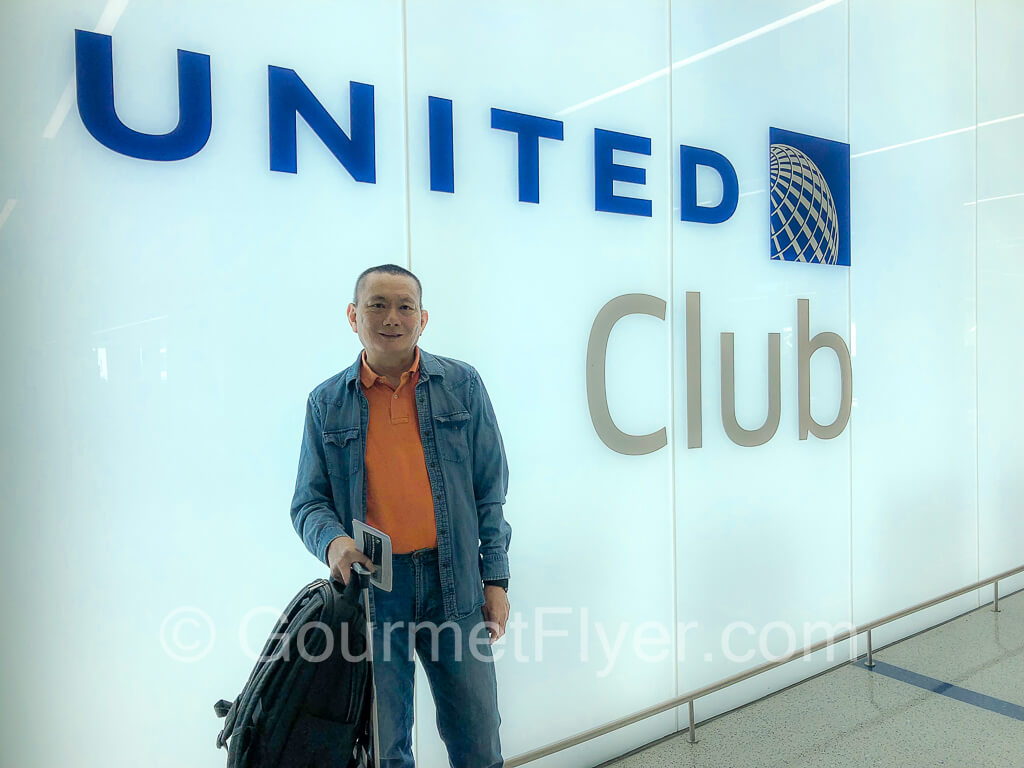The Gourmet Flyer posing in front of the large floor to ceiling United Club glass panels.