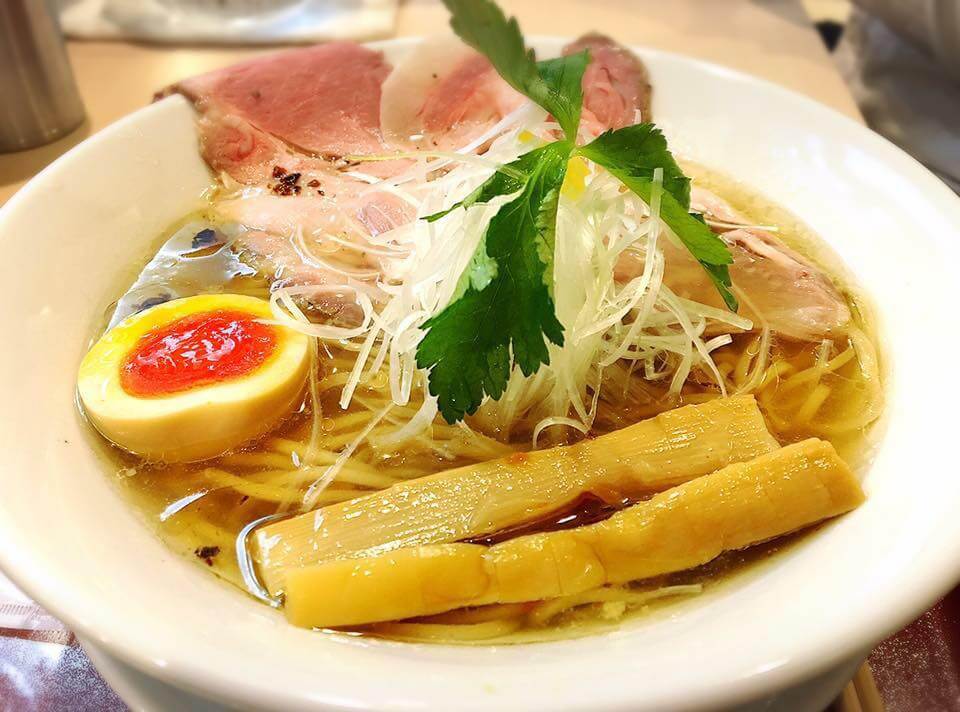 A bowl of ramen topped with slices of duck breast and a half soft boiled egg.