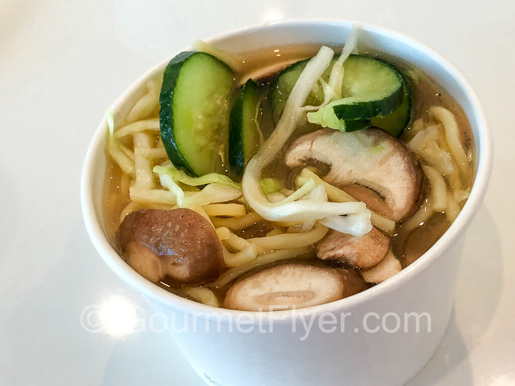 A cup of ramen with cucumbers and mushrooms.