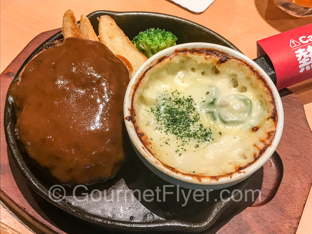 Hamburg steak served on a sizzling platter with gravy and baked macaroni.