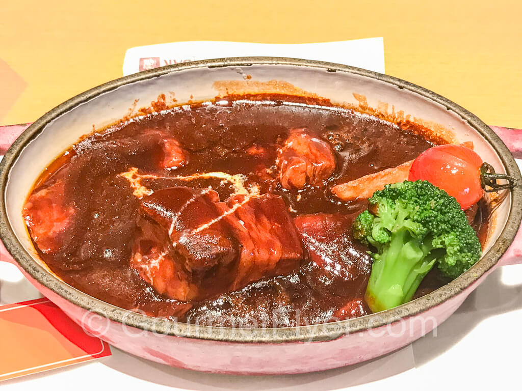 Beef stew served with lots of gravy and a piece of broccoli.