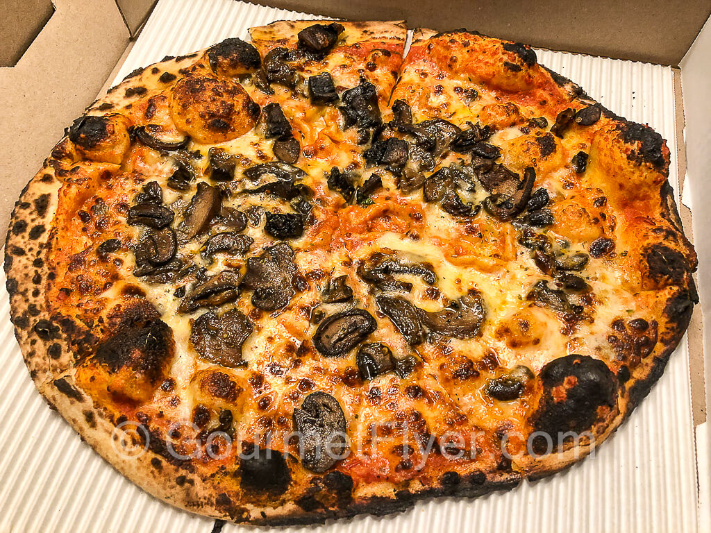 A 12-inch wood-fired pizza with a slightly burnt crust topped with portobello mushrooms.