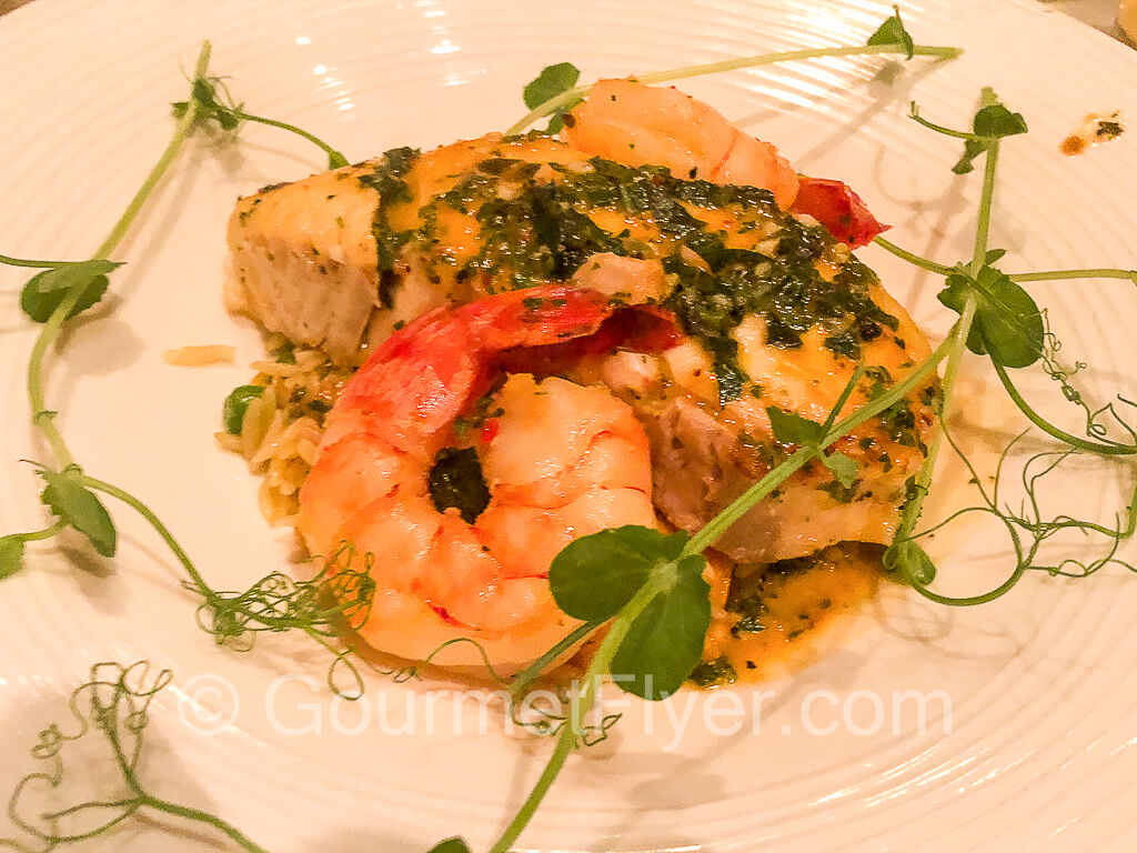 A thick halibut steak on a plate accompanied by two large prawns.
