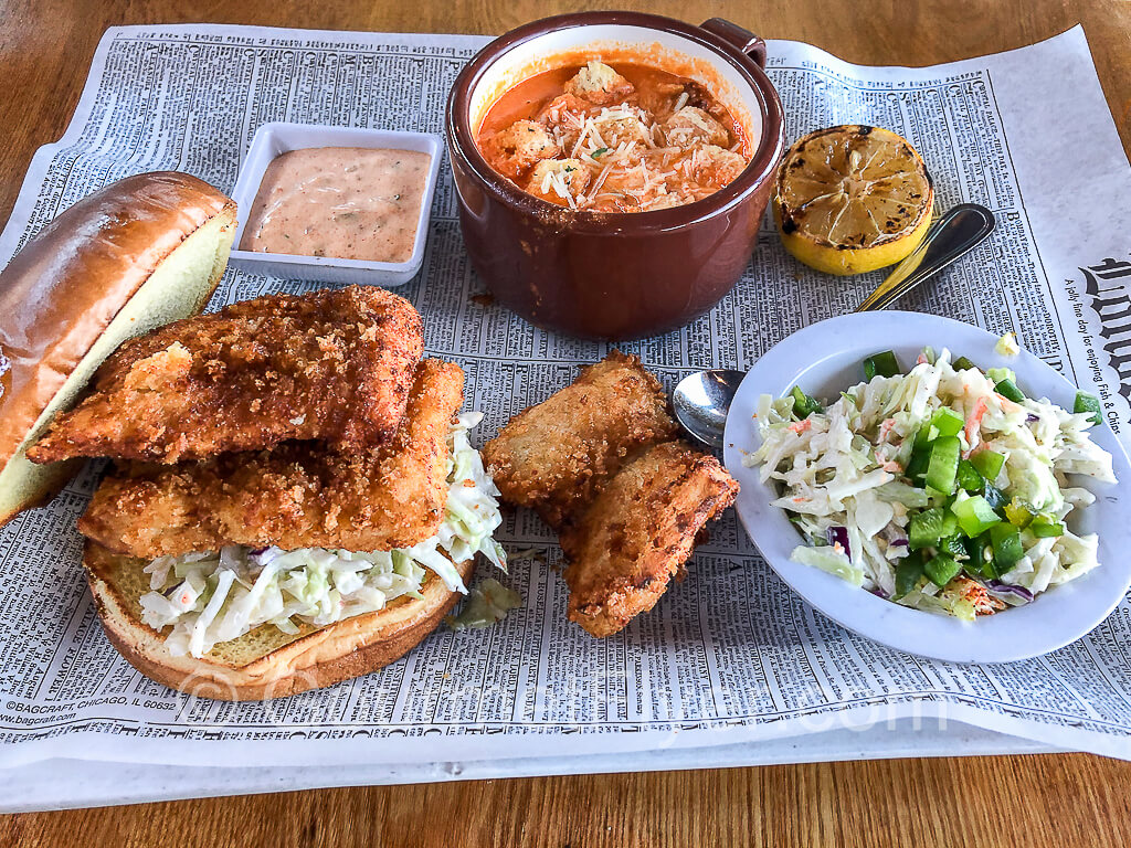 A tray with a fish sandwich, jalapeño slaw, and a cup of tomato soup. 