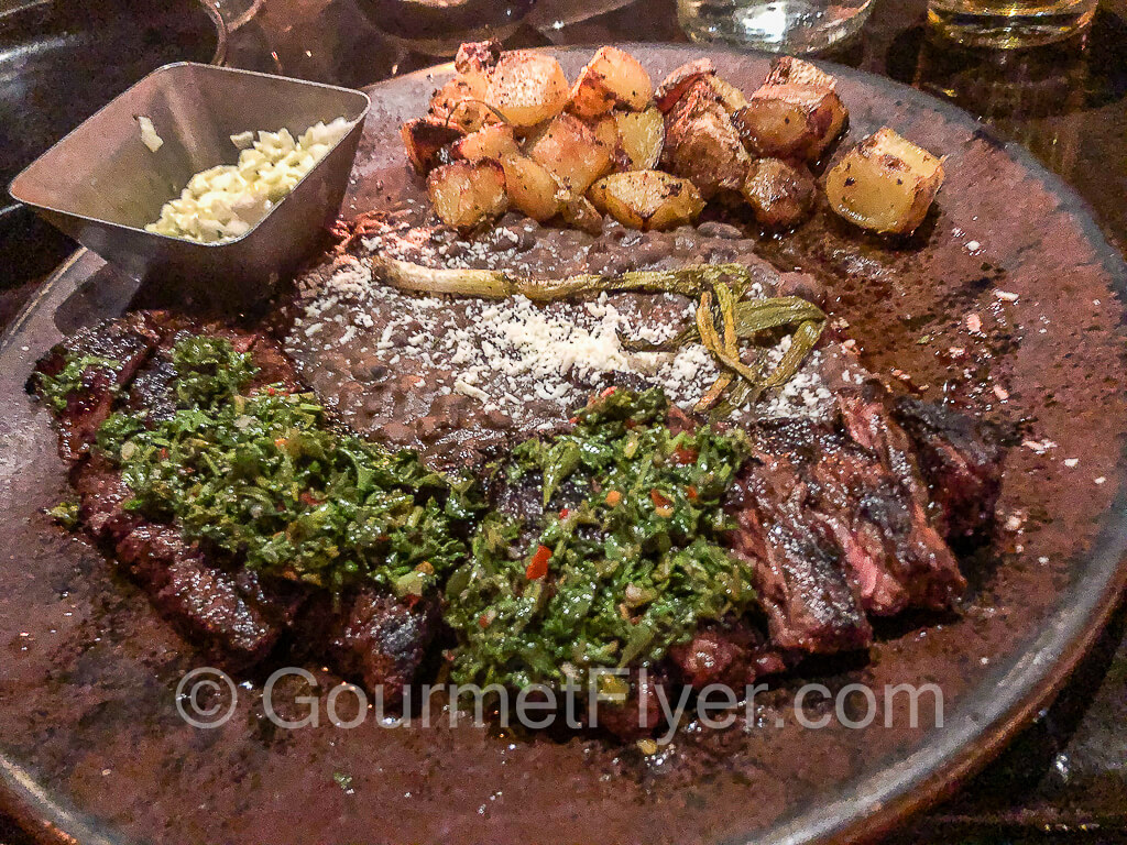 Cubano skirt steak is sliced, topped with chimichurri, and served with roasted potatoes.