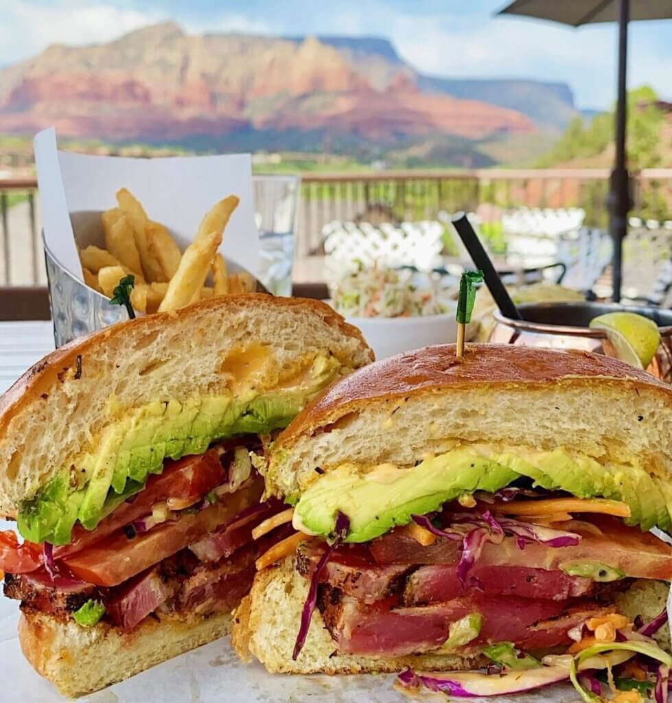 A sandwich with meats. tomatoes, and avocado with the red rocks in the background.