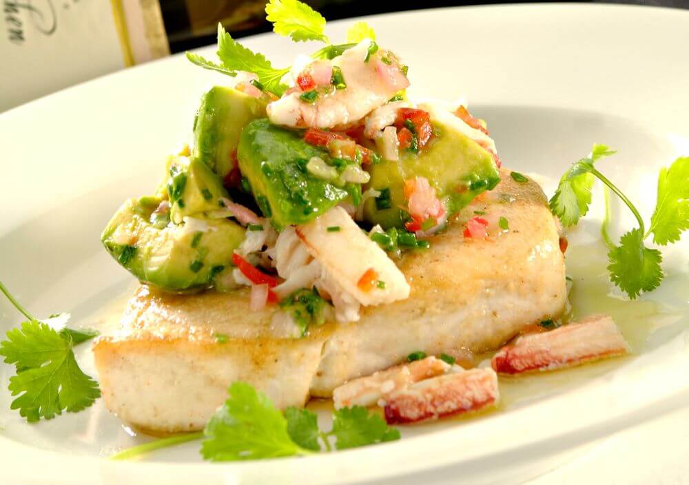 A sauteed fish filet topped with avocado and garnished with parsley. 