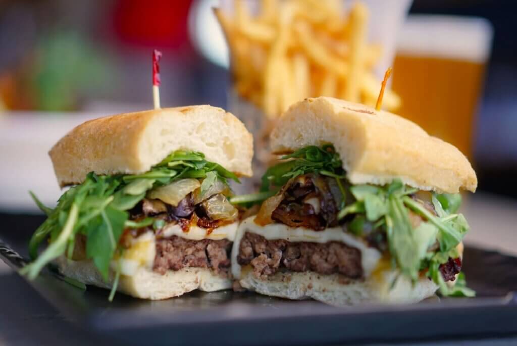 A mushroom burger sandwiched in a bolillo bun with French fries in the background.
