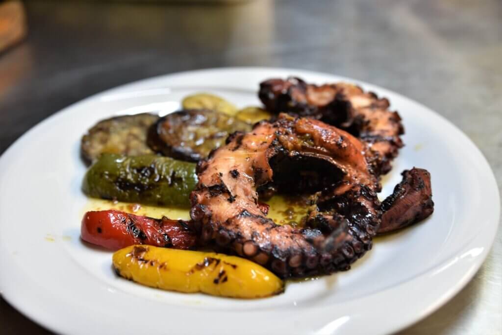 A plate with a grilled octopus accompanied by sauteed vegetables.