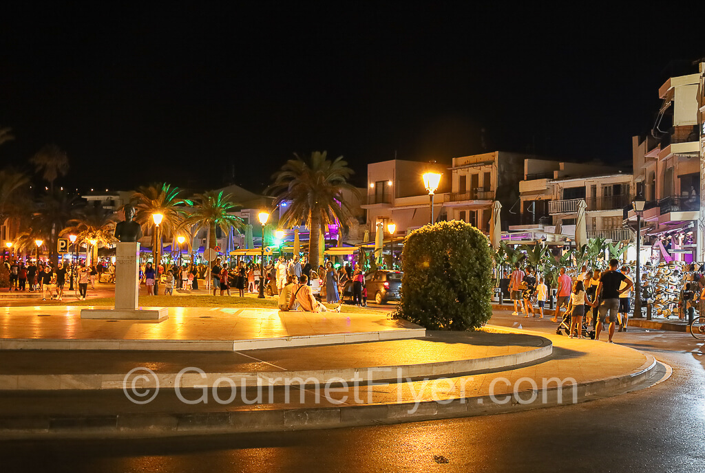 A vibrant night scene at a circular square featuring a sculpture at its center.