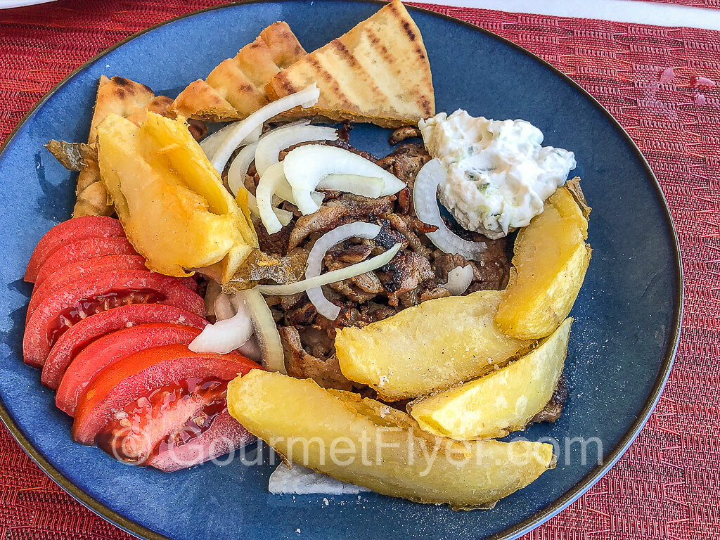 A plate of gyro with pita bread, slices tomatoes, and French fries.