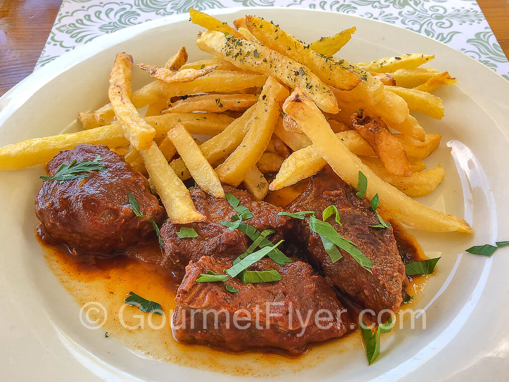 Beef cooked in tomatoes is served on a plate with French fries.