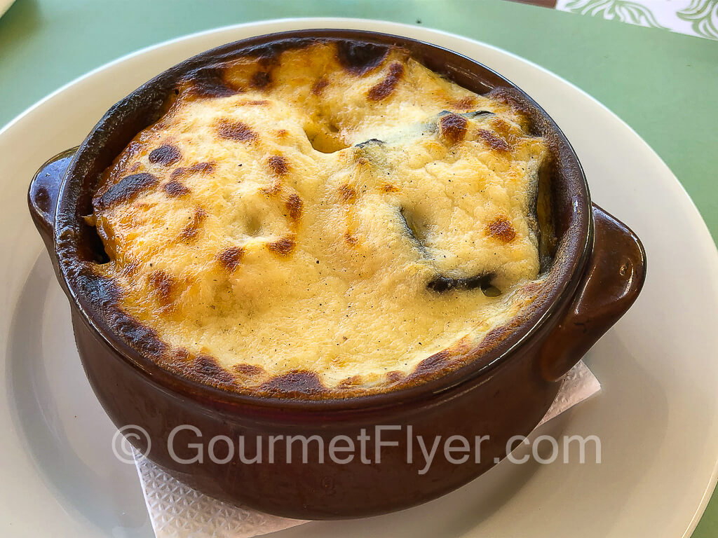 A large ceramic soup bowl is topped with melted cheese that is sightly burnt in various spots.
