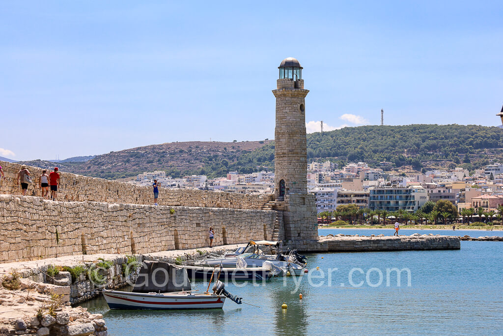 The lighthouse and breakwater sit atop the waters with the hilly island in the background.