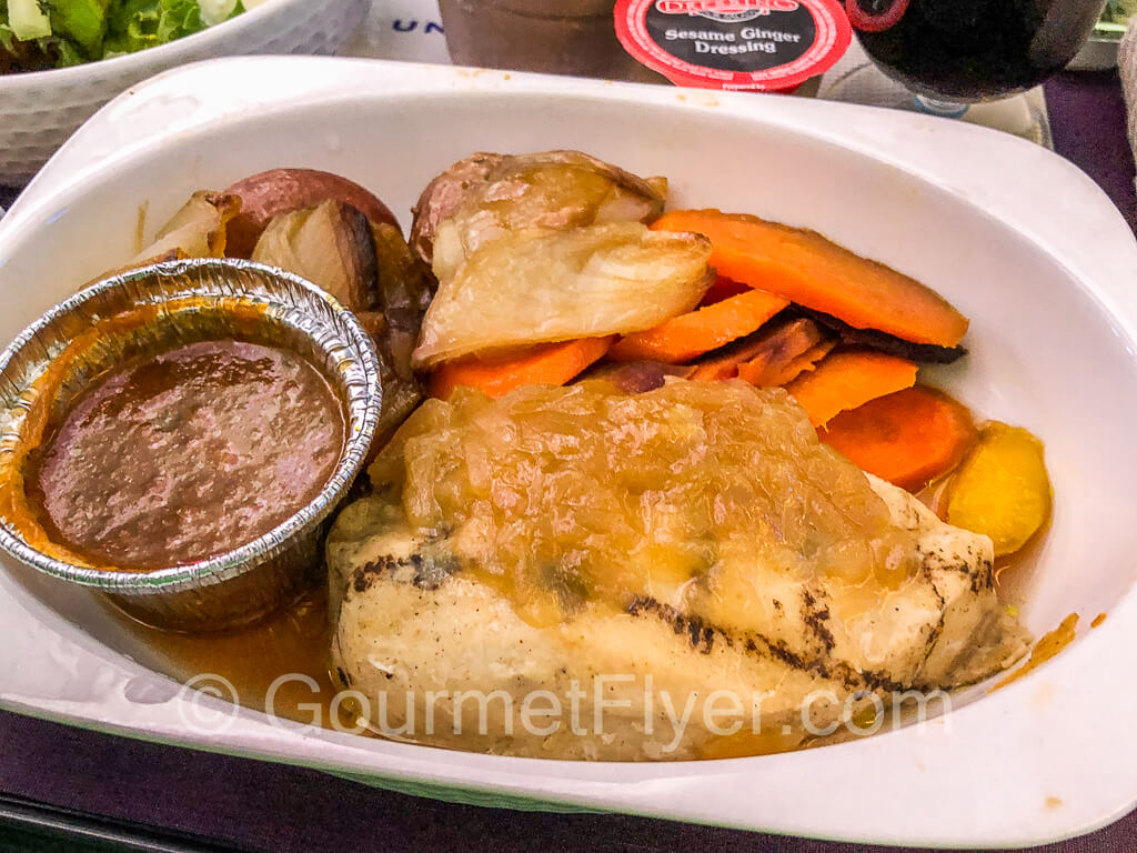 A plate with a grilled chicken breast, gravy, and side dishes.