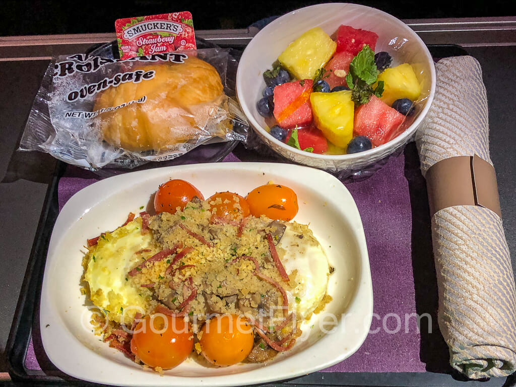 United Premium Plus breakfast tray with baked eggs, mushrooms, bacon, and grape tomatoes. Served with fruits and a pastry.