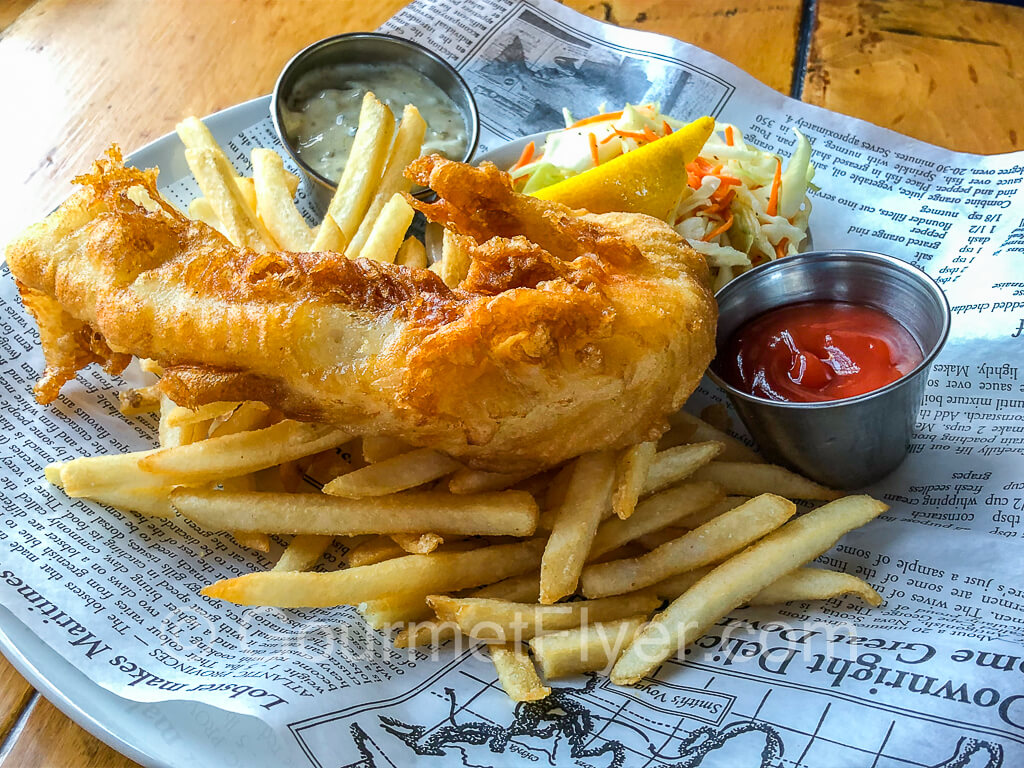 A piece of golden-brown fish served with French fries, tartar sauce, and ketchup.