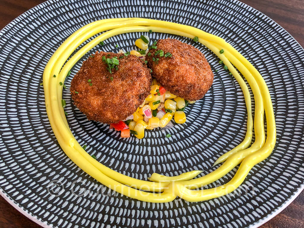Two crab cakes garnished with a circle of saffron aioli.