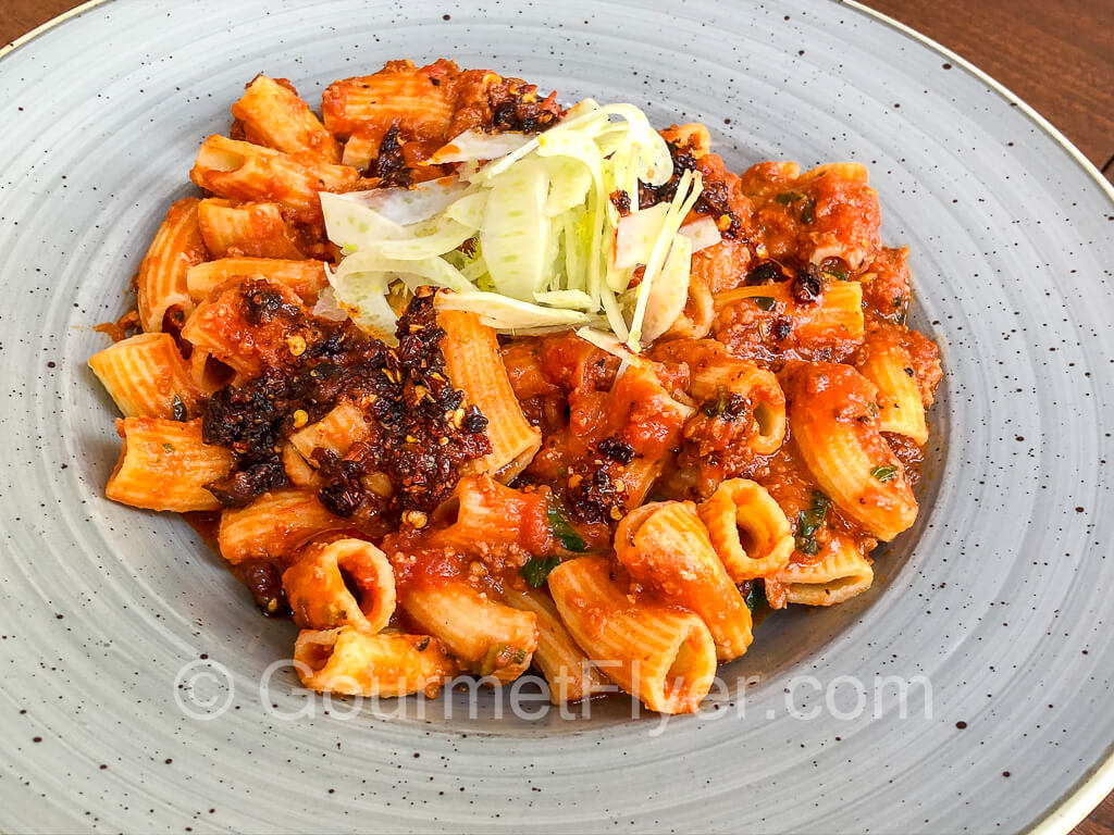 A plate of rigatoni with a red sauce and garnished with red chili flakes.