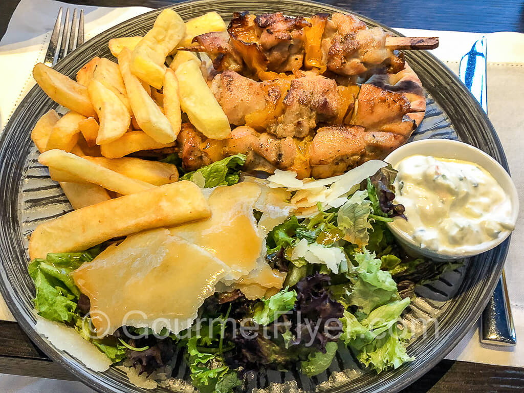 A plate of chicken skewers served with fires and garnished with a salad.