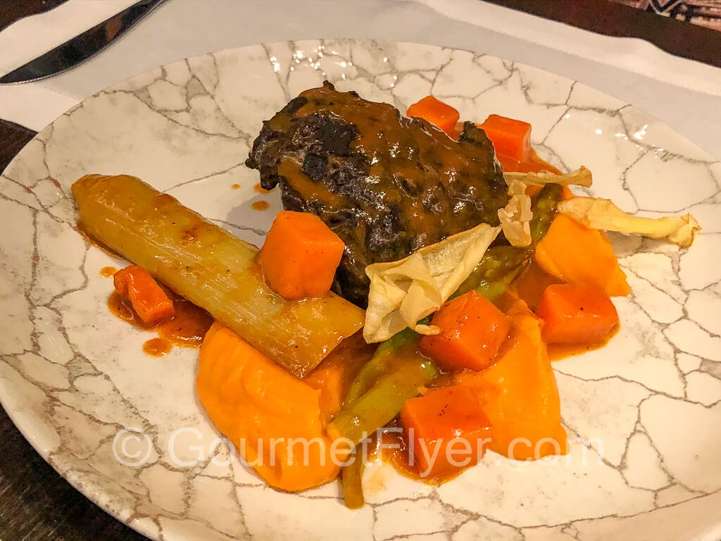 Braised beef cheeks served with carrots and vegetables.