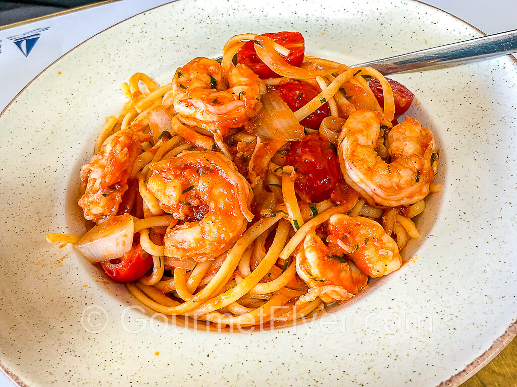 A dish of linguini with shrimps and garnished with cherry tomatoes.