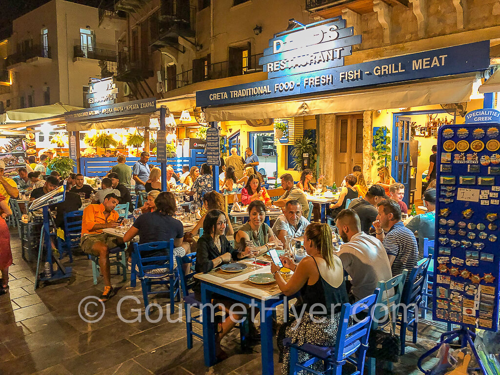 Many customers are seated in the outdoor dining area of a restaurant during a vibrant night scene.