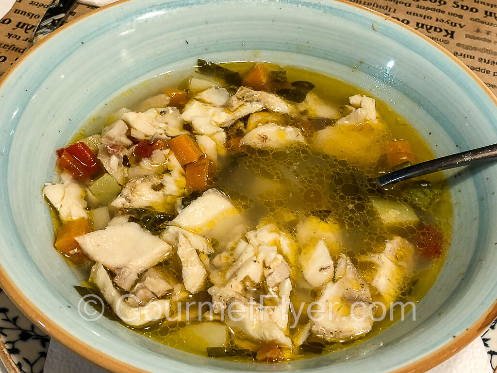 A bowl of fish soup with pieces of fish filets.