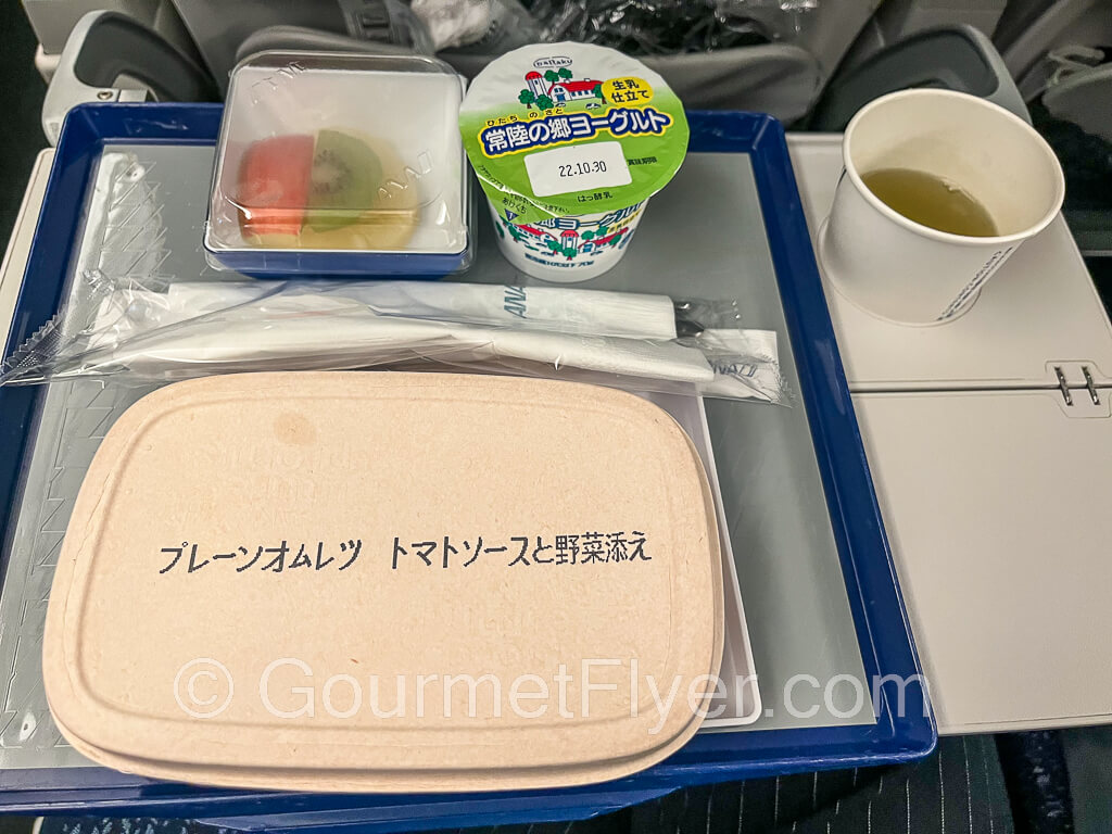 Breakfast tray with fruits, yogurt, and a covered entree.