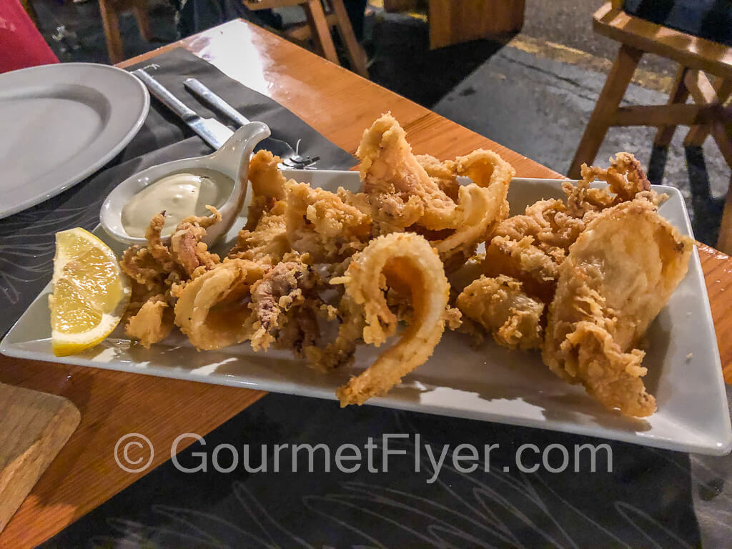 A plate of fried calamari served with a lemon wedge and mayonnaise.