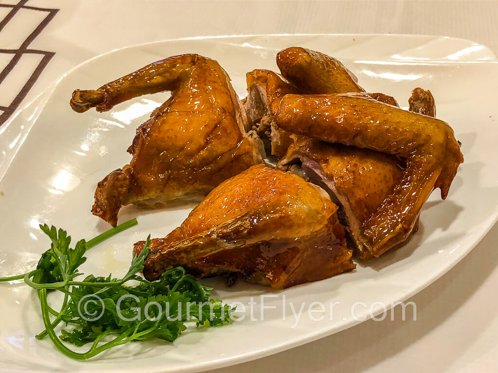 A roasted squab cut into four quarters and served on a plate, garnished with cilantro.