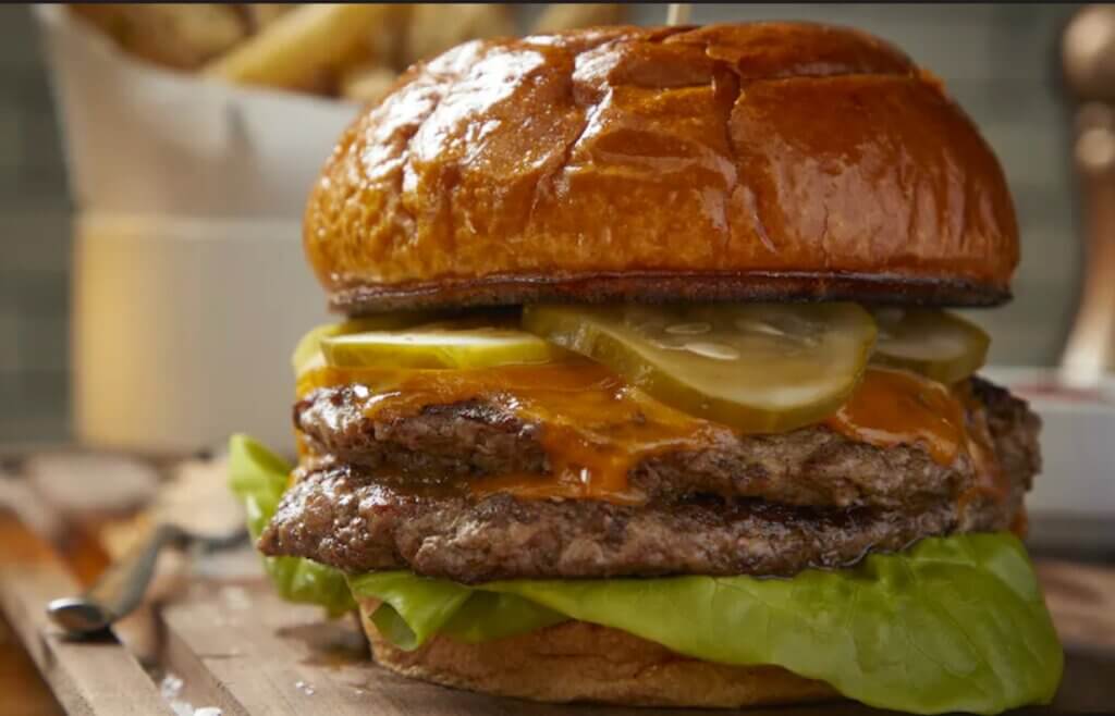 A burger with two beef patties and garnished with pickles, lettuce and a red sauce.