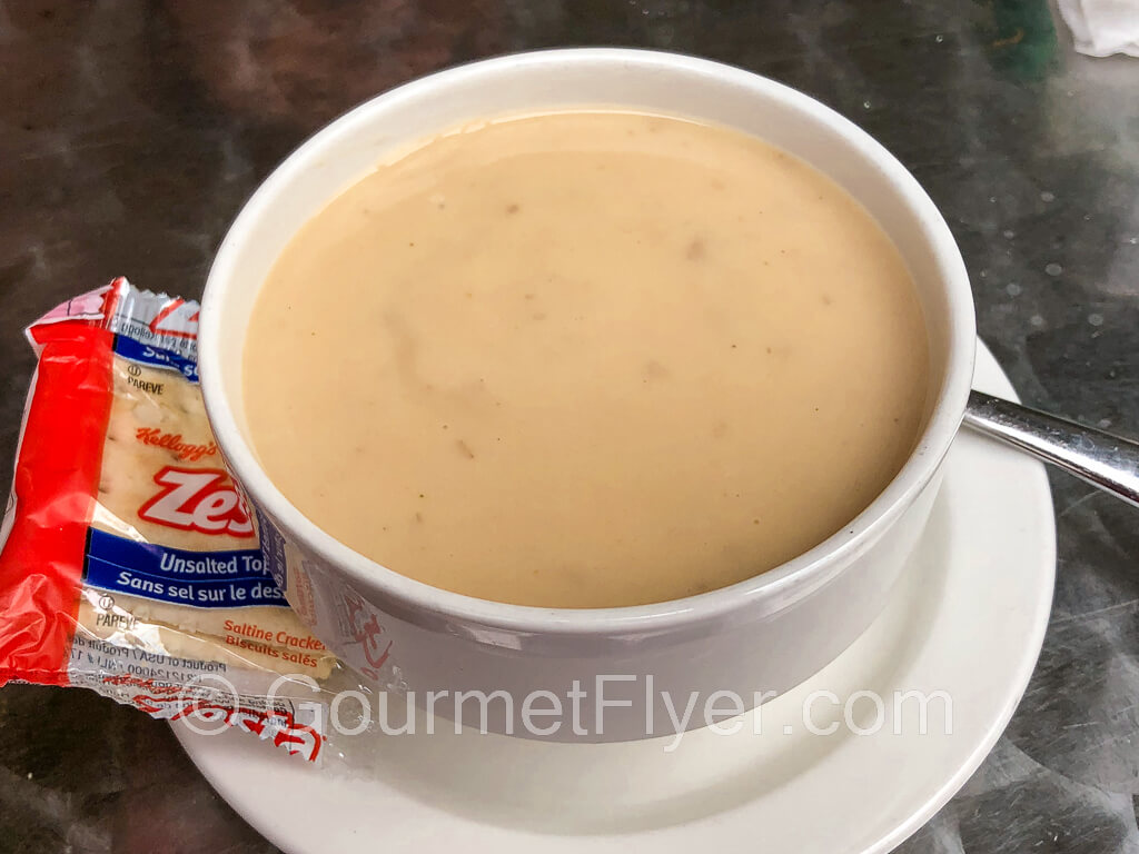 A bowl of cream of mushroom soup on a plate with a packet of crackers on the side.