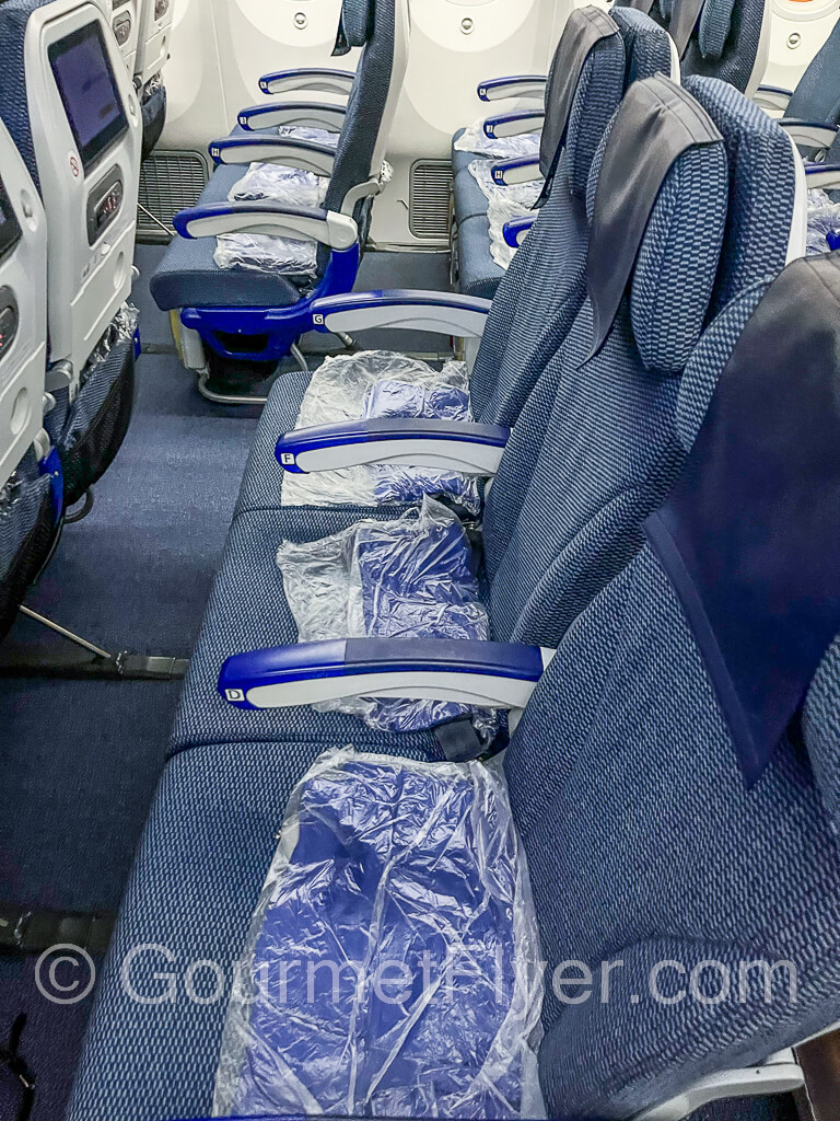 Rows of seats in the window section and the middle section of the plane. Blankets are placed on the seats.