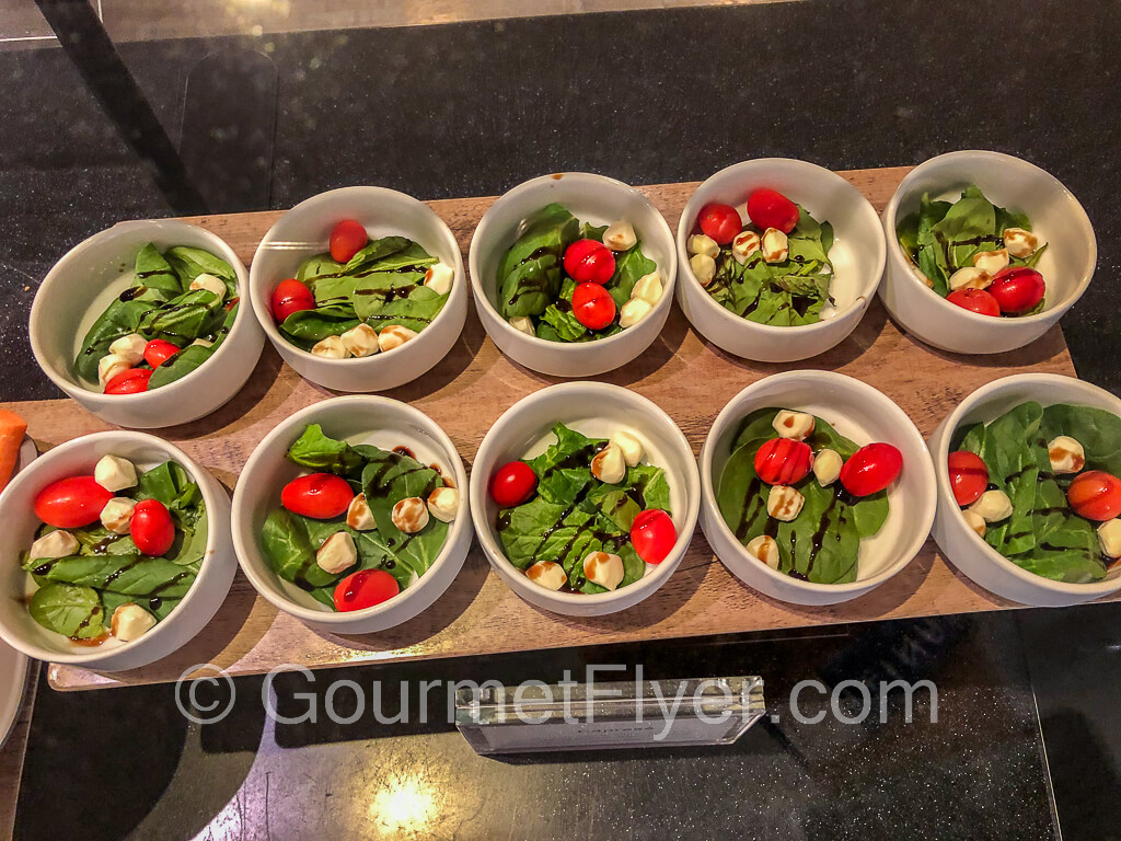 Two rows of salad bowls containing fresh mozzarella, tomatoes, and fresh basil.