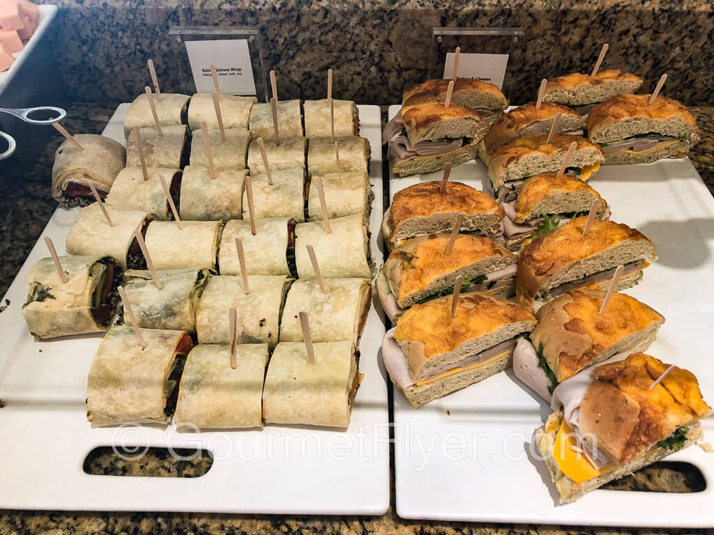 A platter of white tortilla rolls is on the left and a platter of cut sub sandwiches is on the right.