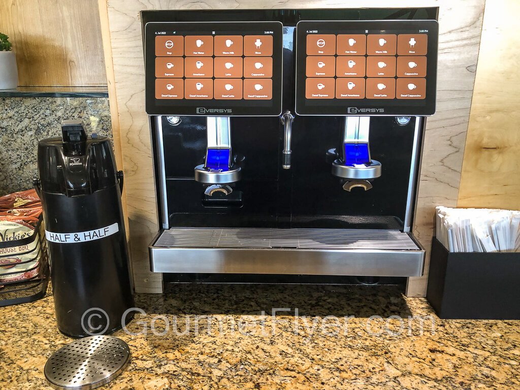 Two espresso machines are placed side by side with a container of half and half to the left.