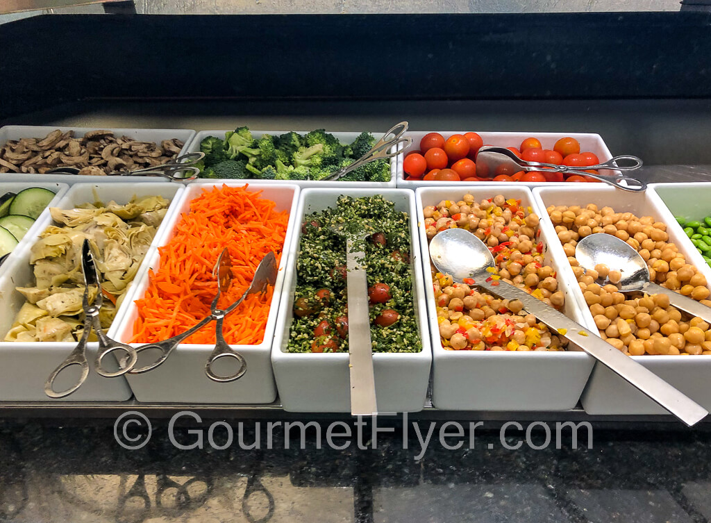 Salad bar with a variety of vegetables, such as broccoli, cherry tomatoes, beans, shredded carrots, etc. in individual serving trays.