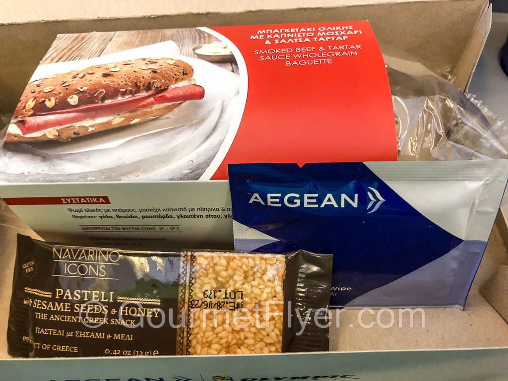 A lunch box containing a baguette sandwich in a box and a honey sesame bar.