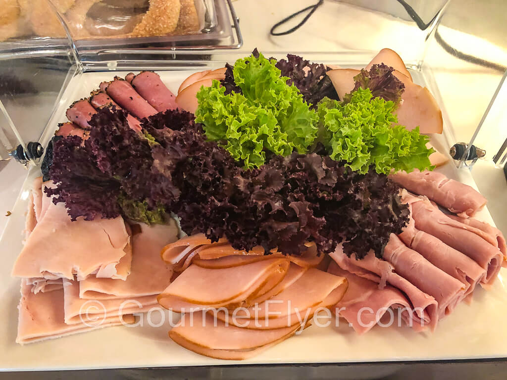 A deli meat platter garnished with green and purple lettuce leaves.